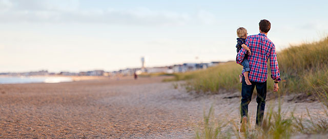 Man med barn på höften, gående på strand