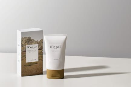 En tub med Skin1004 Centella hudvårdsprodukt står bredvid sin förpackning på ett vitt bord. Förpackningen har ett landskapsmotiv, och produkten har en enkel etikett med vit text.