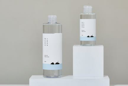 Två RoundLab hudvårdsflaskor står på vita block framför en neutral bakgrund. Flaskorna har minimalistiska etiketter med bergsikoner och en ljusblå färgdetalj.