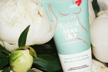 FemCare Natural Moist Glide från RFSU liggande bland vita pioner och gröna blad.