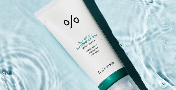 En vit tub med Dr. Ceuracles Cica Regen Waterproof Sun SPF50+ med en liggande på en bakgrund av blått vatten.