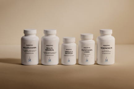 Fem flaskor med Holistic kosttillskott (Multivitamin, Multi-Mineral, Omega-3 Algeolja, D3-Vitamin 2000 och Magnesium) med vita etiketter, alla förpackade i vita plastflaskor. Flaskorna är arrangerade på en beige yta.