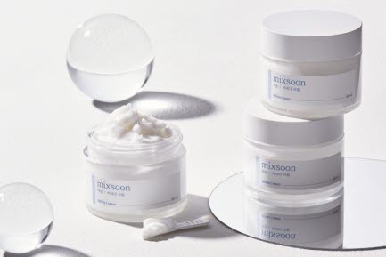 Två burkar med Mixsoon hudkräm staplade ovanpå varandra och en öppen burk med kräm på en spegelplatta. Runt produkterna finns dekorativa genomskinliga sfärer.