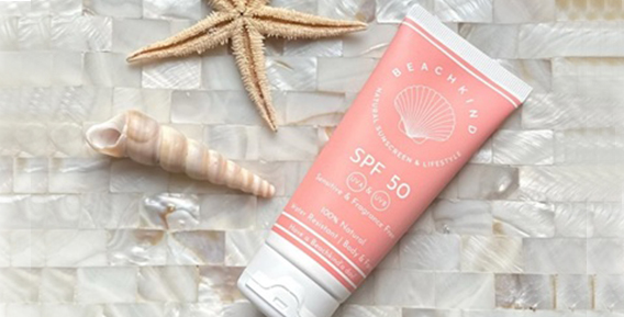 En aprikosfärgad tub med solskydd spf 50 från Beachkind. Ligger mot en bakgrund i sten. Till vänster i bild syns både en snäcka och en sjöstjärna.